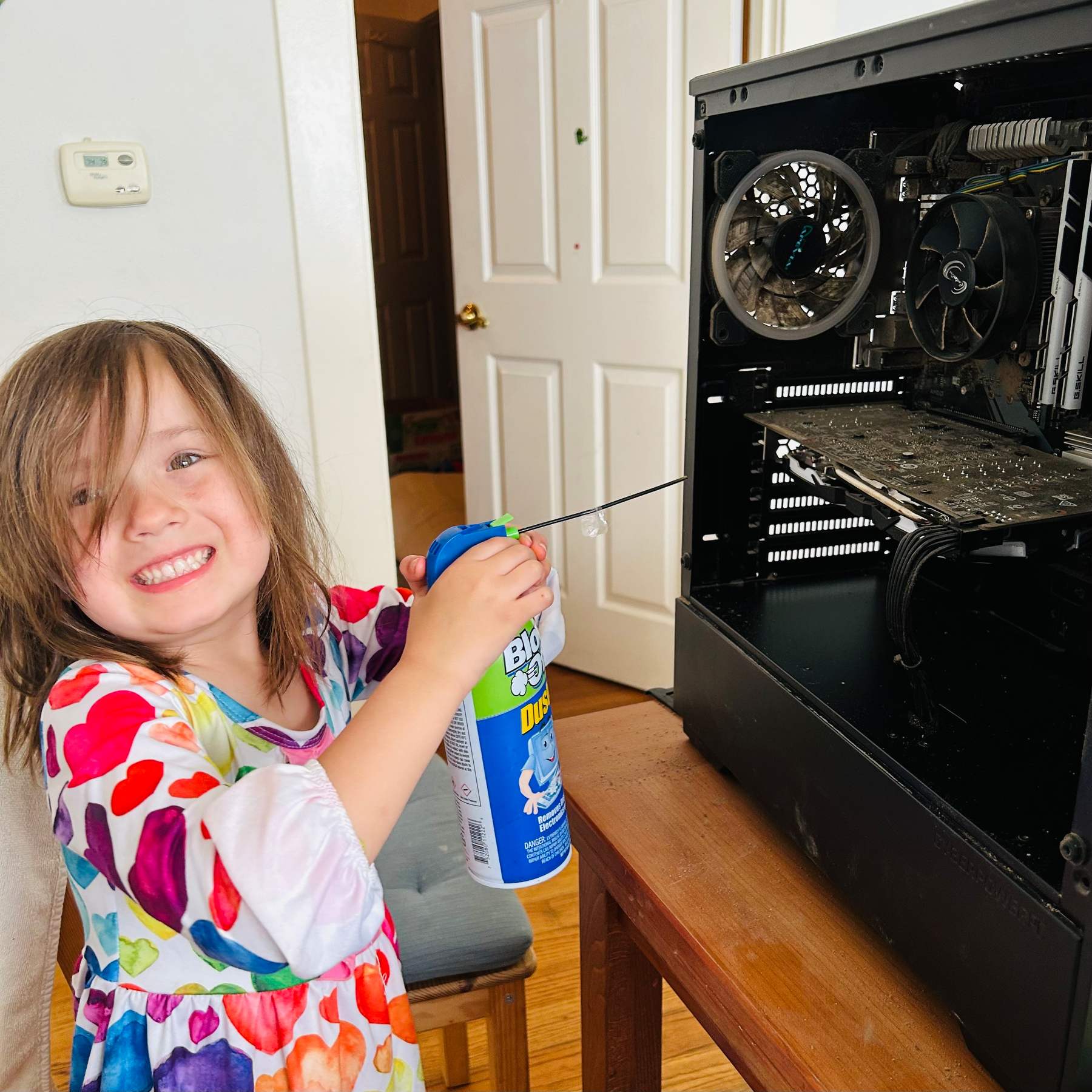 A child smiling while holding a can of compressed air next to an open computer case.