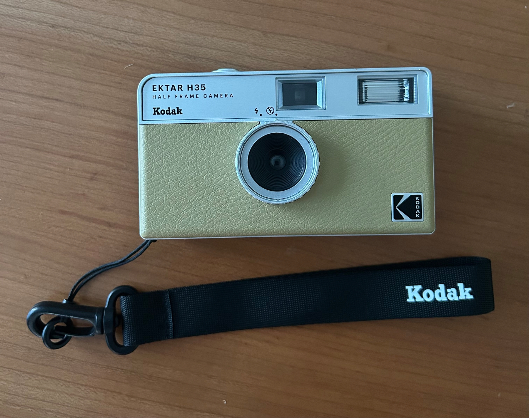 A Kodak Ektar H35 half-frame camera with a wrist strap is placed on a wooden surface.