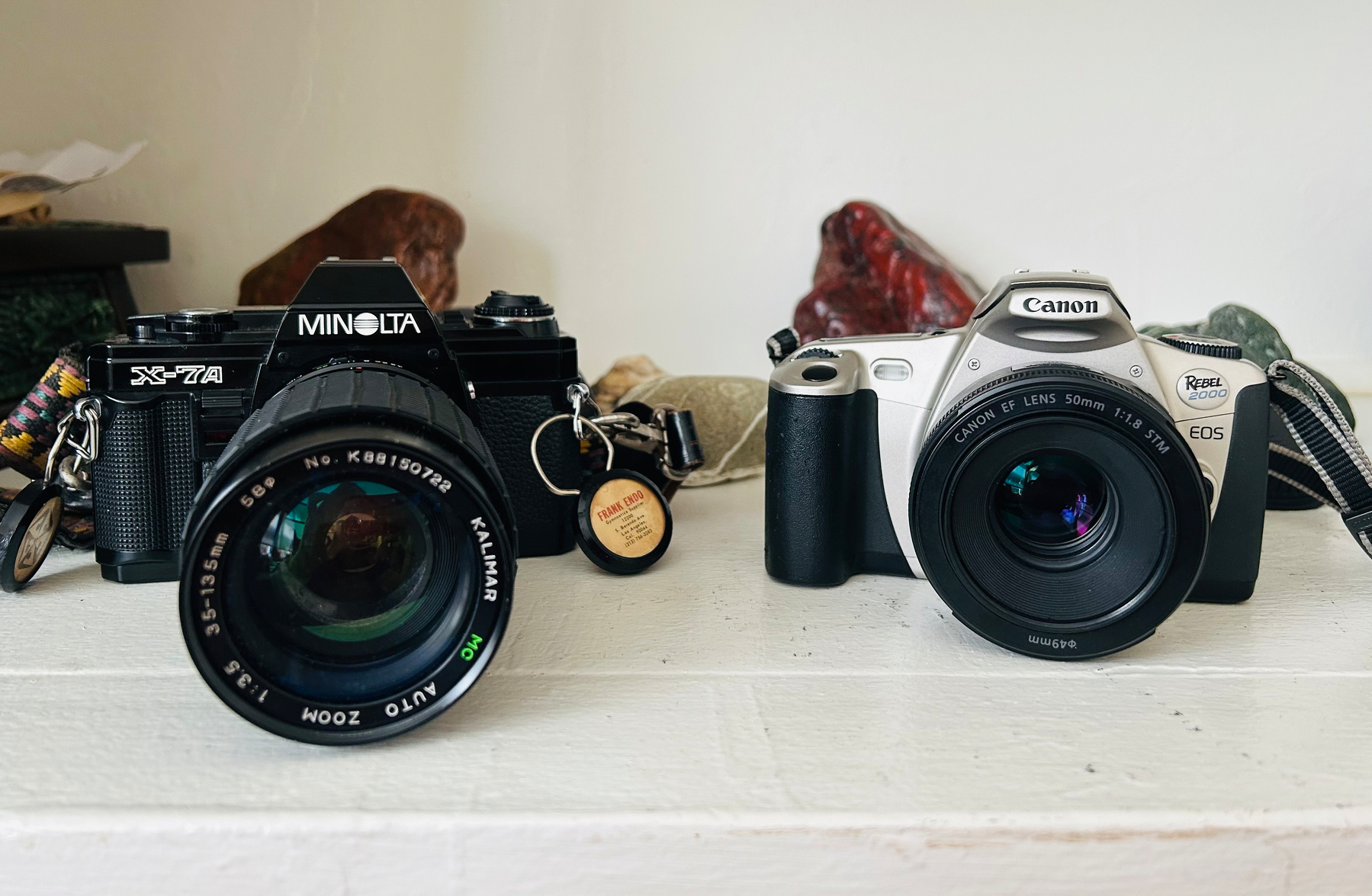 Two vintage cameras, a black Minolta and a silver Canon, are placed side by side on a white surface.
