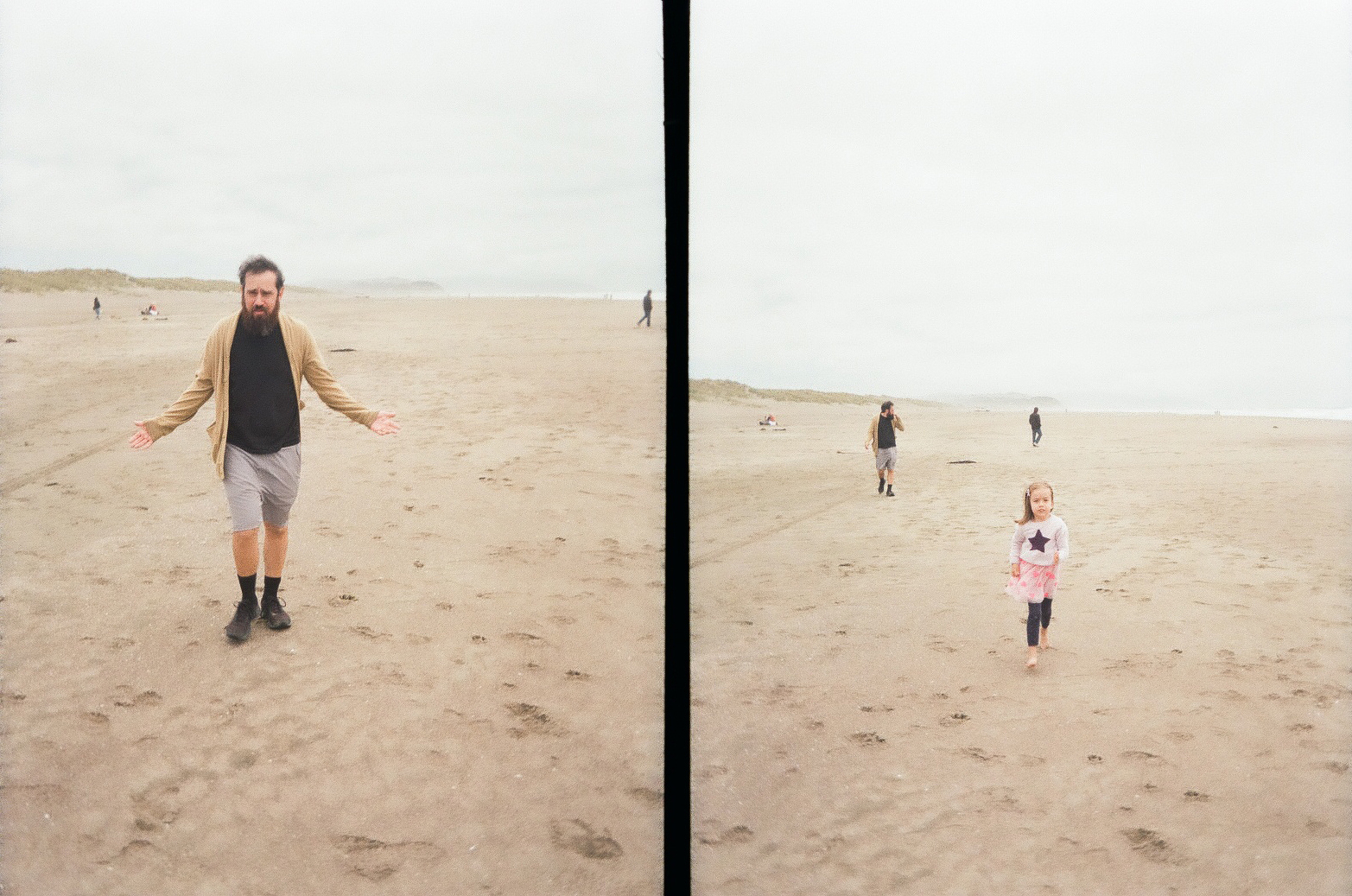 A man and a child are walking separately on a wide, empty sandy beach with a few other people in the distant background under an overcast sky.
