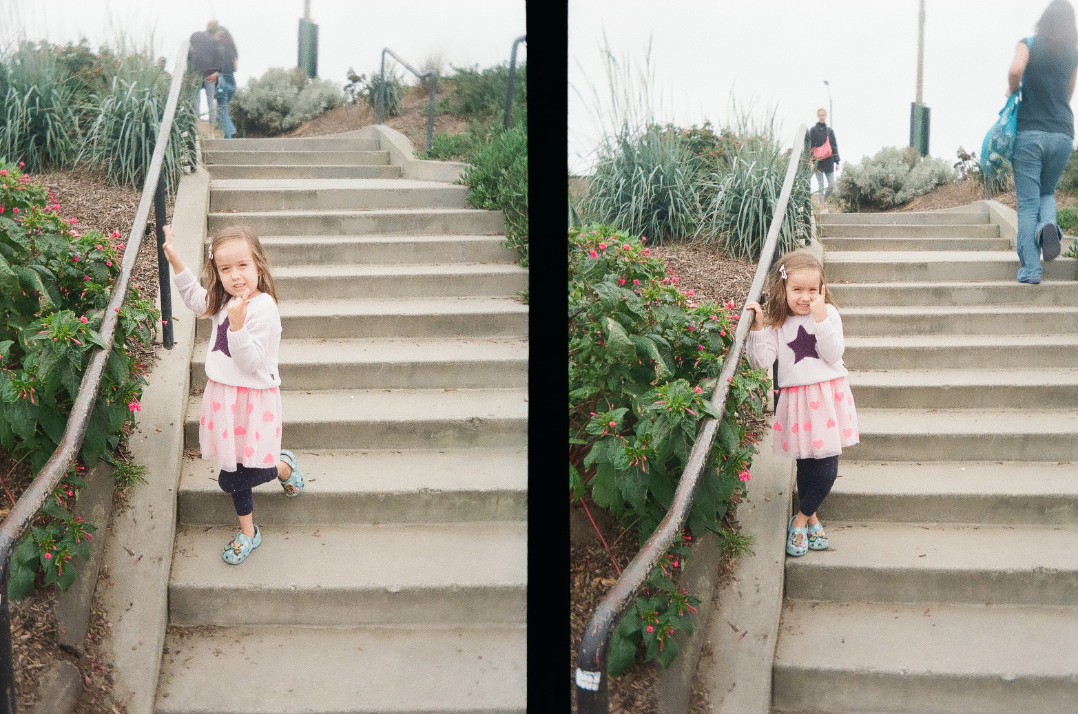 A young girl in a pink skirt and star sweater is standing on outdoor concrete stairs, holding a railing and smiling at the camera.