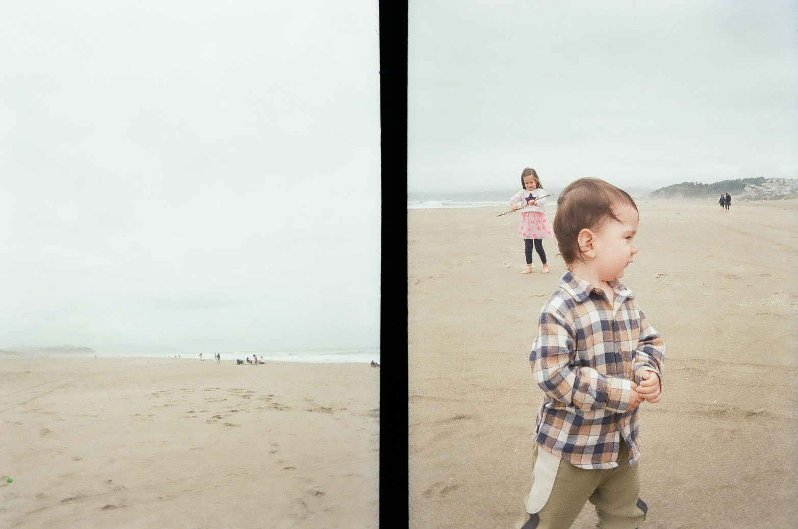 Two children are playing on a sandy beach on a cloudy day, with one child closer to the camera and another in the background.