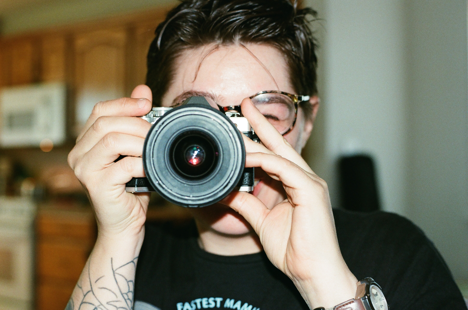 A person with short hair and glasses is holding a camera up to their face, ready to take a photo.